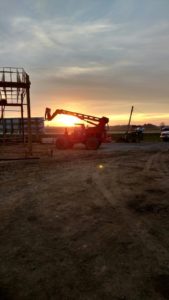 Workers at the Alt Oil Company jobsite capture a beautiful sunset behind a piece of machinery after a long day of work.